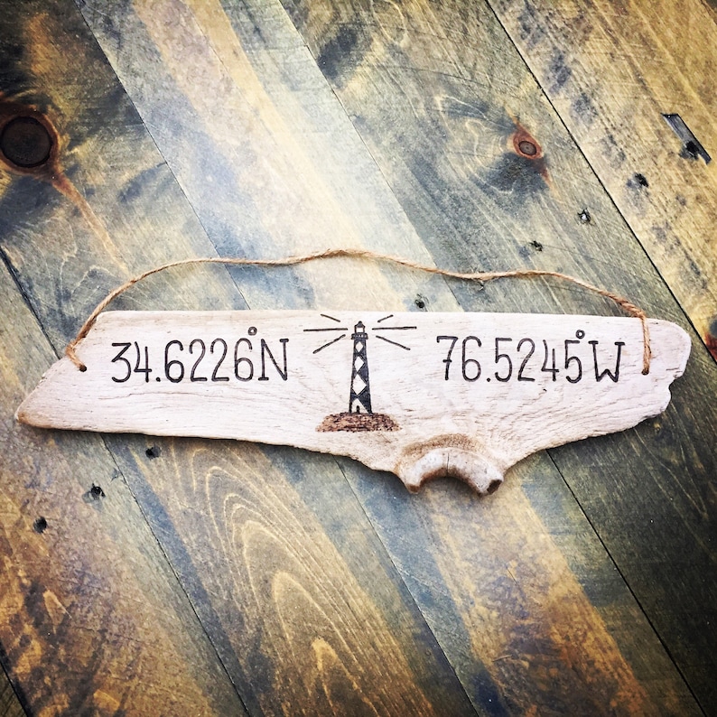 May include: A piece of driftwood with the coordinates 34.6226&deg;N 76.5245&deg;W and a lighthouse illustration burned into the wood.