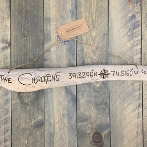 May include: A piece of driftwood with the text "The Chaikens 39.3296°N 74.5160°W Est. 2016" burned into it. The driftwood is hanging from a string and has a compass symbol burned into it.