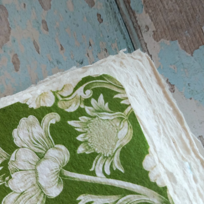 May include: A stack of thick, off-white handmade paper with rough, deckled edges. The top sheet features a vibrant green background printed with a detailed white floral pattern consisting of large blossoms, buds, and leafy stems across the surface.