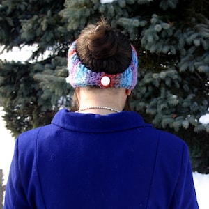 Puede incluir: Una diadema de punto azul con un botón blanco como adorno. La diadema la lleva puesta una persona con una chaqueta azul.