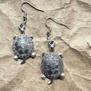 Peut inclure: Une paire de boucles d'oreilles en forme de tortue argentées avec un motif de carapace détaillé. Les boucles d'oreilles ont une fermeture simple à crochet.