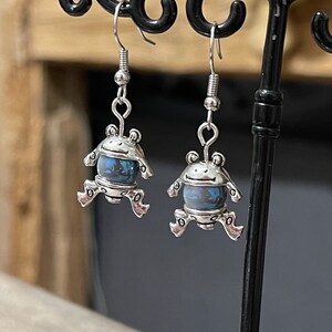 Metal earrings with a small frog and a blue-grey magic bead
