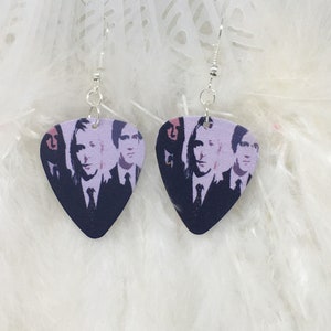Può includere: Un paio di orecchini d'argento con un design a forma di plettro per chitarra viola che presenta una band di quattro uomini in bianco e nero.