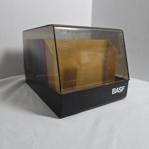 May include: A black and clear plastic display case with the word "BASF" printed in white on the front. The case has a hinged, clear top and contains several colored cards. The case is rectangular.