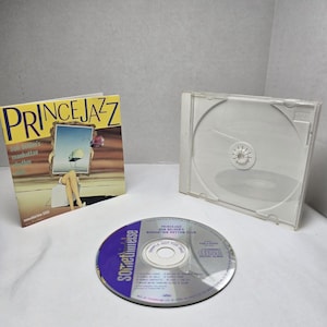 May include: A Prince Jazz Bob Belden's Manhattan Rhythm Club music CD with a clear plastic jewel case and a square paper insert. The insert features a surreal illustration of legs and a floating frame against a yellow and brown background.