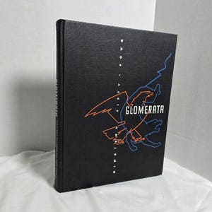 May include: A hardcover book with a black cover featuring the word "GLOMERATA" in white, and the text "NINETEEN FIFTY FOUR" in vertical orange and blue. The book has a textured appearance.
