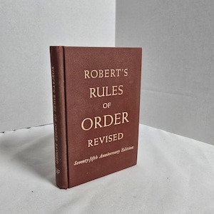 May include: A hardcover book titled "Robert's Rules of Order Revised." The book is a dark reddish-brown color with gold lettering. The spine reads "Robert's Rules of Order Revised." The cover also states "Seventy-fifth Anniversary Edition."