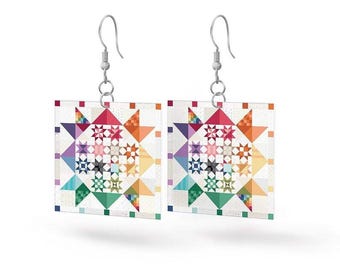 May include: A pair of square earrings with a colorful star quilt pattern. The earrings feature a white background with a geometric design in shades of red, orange, yellow, green, blue, and purple. The earrings hang from silver-colored hooks.