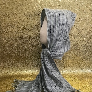 Può includere: Una sciarpa con cappuccio a righe grigie e bianche con frange. La sciarpa è realizzata in un tessuto morbido e tessuto.