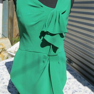 May include: A sleeveless emerald green dress with a bow detail at the neckline. The dress has a fitted bodice and a flowing skirt.