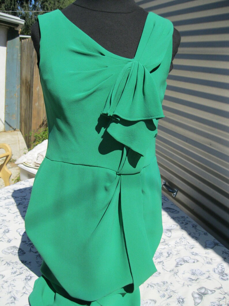 May include: A sleeveless emerald green dress with a bow detail at the neckline. The dress has a fitted bodice and a flowing skirt.