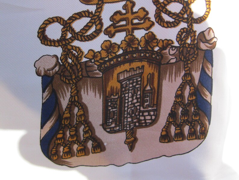 May include: A detailed illustration of a coat of arms with a gold rope border, a gold cross, a gold castle, and gold tassels. The castle is on a tan background with a blue and white striped border.