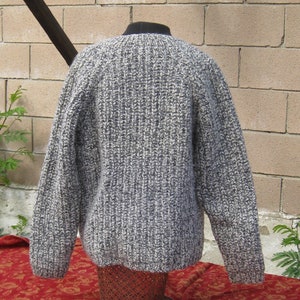May include: A gray and white knit sweater with a ribbed texture. The sweater has long sleeves and a crew neck. The garment is displayed on a mannequin. The sweater is made of a thick, warm yarn, perfect for cooler weather.