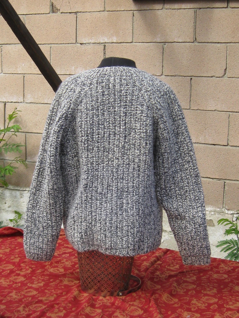 May include: A gray and white knit sweater with a ribbed texture. The sweater has long sleeves and a crew neck. The garment is displayed on a mannequin. The sweater is made of a thick, warm yarn, perfect for cooler weather.