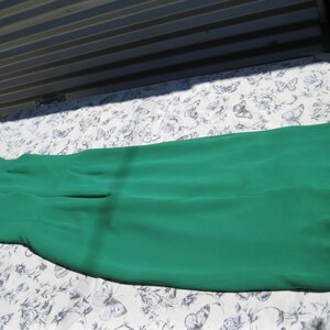 May include: A long, emerald green maxi skirt made of a soft, flowing fabric. The skirt is laid flat on a white background with a floral pattern.