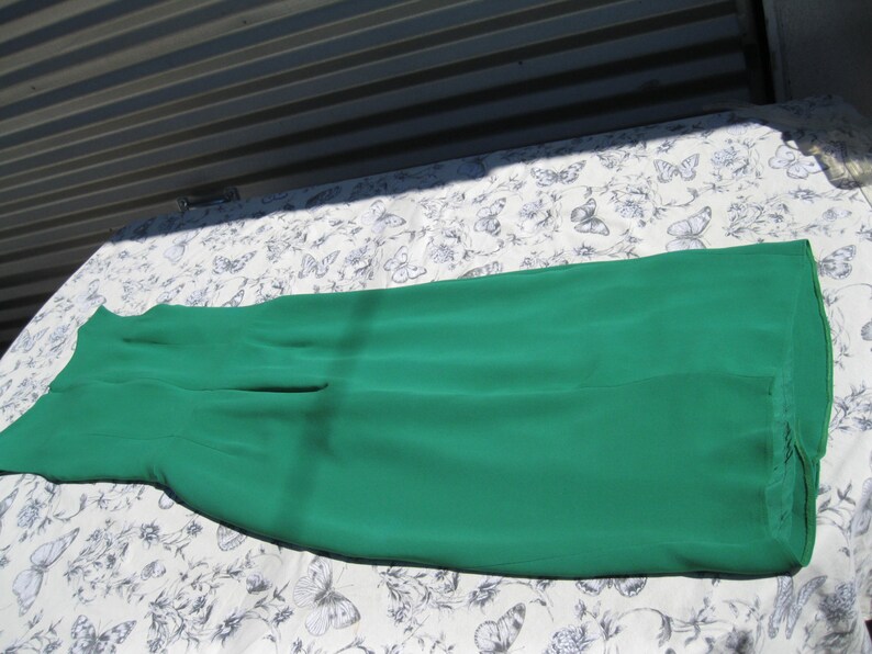 May include: A long, emerald green maxi skirt made of a soft, flowing fabric. The skirt is laid flat on a white background with a floral pattern.