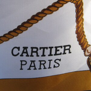 May include: A white silk scarf with a brown rope design and the text 'CARTIER PARIS' in black lettering.