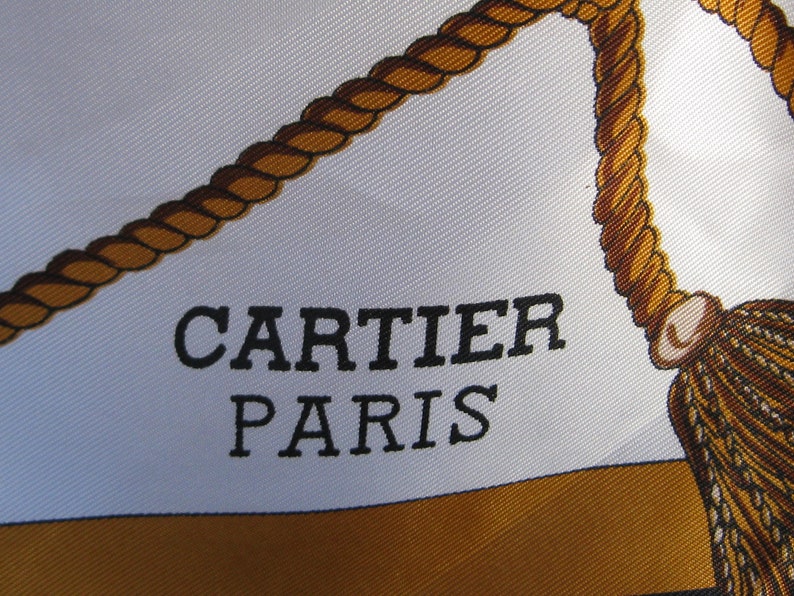May include: A white silk scarf with a brown rope design and the text 'CARTIER PARIS' in black lettering.