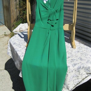 May include: A green sleeveless dress with a bow at the neckline. The dress is hanging on a wooden rack.