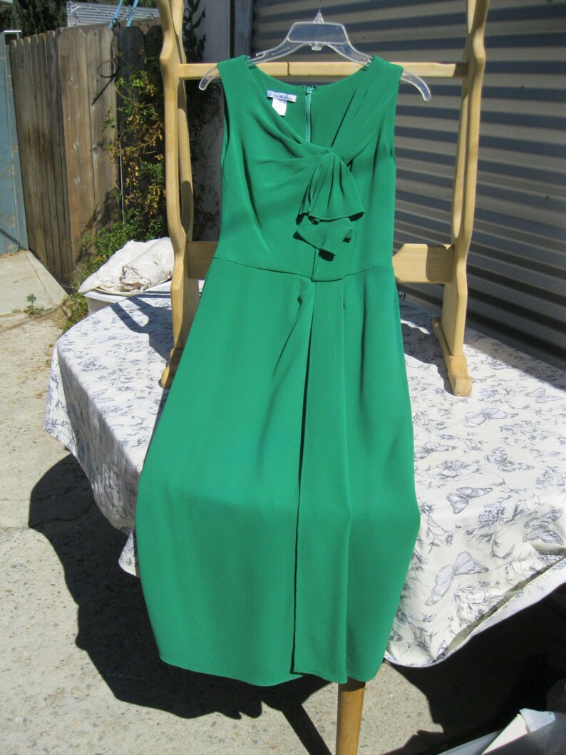 May include: A green sleeveless dress with a bow at the neckline. The dress is hanging on a wooden rack.
