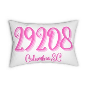 Könnte beinhalten: Weißes rechteckiges Kissen mit dem rosa Text "29208" und "Columbia SC" in Schreibschrift. Die Zahlen haben einen geschichteten Schatteneffekt. Ein Einrichtungsgegenstand.