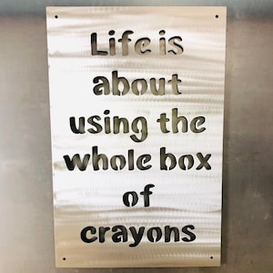 May include: A metal sign with the quote "Life is about using the whole box of crayons" cut out of the metal.