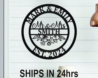 May include: Black metal sign with the text "Mark & Emily Mr & Mrs Smith Est. 2024" in a circle with floral accents. The sign is on a white wood background.