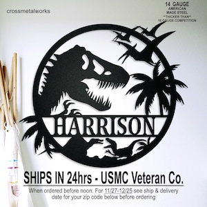 May include: Black metal wall art featuring a dinosaur silhouette within a circular frame. The design includes palm trees, pterodactyls, and the name "HARRISON". The text "14 GAUGE AMERICAN MADE STEEL" is also present.