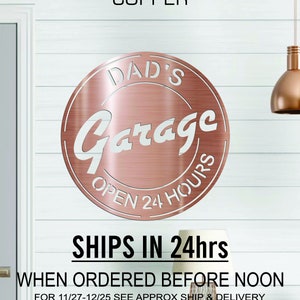 Pode incluir: Placa de metal de cobre com o texto "DAD'S Garage OPEN 24 HOURS" em um c&iacute;rculo branco. A placa tem um acabamento em ouro rosa.