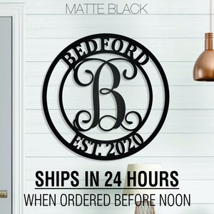 May include: Matte black metal monogram sign with the name "Bedford" and the initial "B" in a decorative script font. The sign also includes the text "Est. 2020".