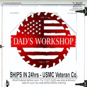 Op de afbeelding: Een rood metalen bord met de tekst "DAD'S WORKSHOP" in een gestileerd lettertype. Het bord heeft de vorm van een zaagblad en toont het ontwerp van de Amerikaanse vlag. Het bord is gemaakt van 14 gauge Amerikaans staal.