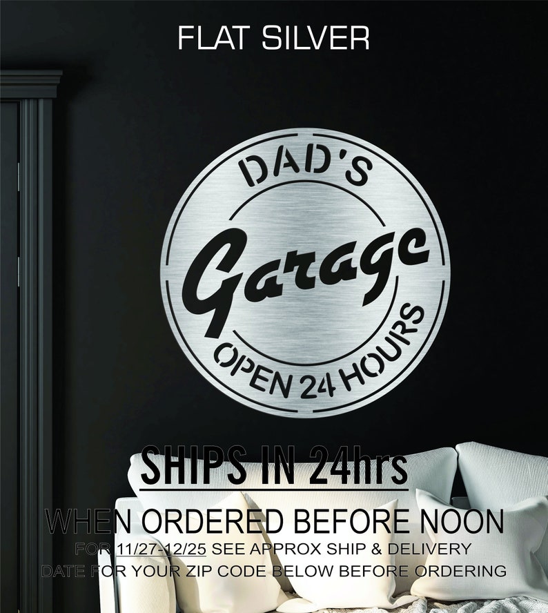 Pode incluir: Um sinal de metal prateado com o texto "DAD'S Garage OPEN 24 HOURS" em um c&iacute;rculo. O sinal est&aacute; montado em uma parede preta.