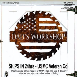 Op de afbeelding: Een metalen bord met een rustieke afwerking, met de tekst "DAD'S WORKSHOP" in vette letters. Het ontwerp bevat de Amerikaanse vlag in een zaagblad vorm. Het bord is gemaakt van 14-gauge Amerikaans staal.