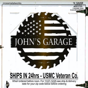 Op de afbeelding: Een zwart metalen bord met de tekst "JOHN'S GARAGE". Het bord heeft een Amerikaans vlagontwerp met sterren en strepen, omlijst door een zaagblad vorm. Gemaakt van 14-gauge staal. Het bord is op een witte deur gemonteerd.