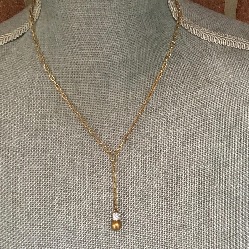 Puede incluir: Un collar tipo lazo en tono dorado con una delicada cadena de eslabones ovalados. El collar tiene un dise&ntilde;o en forma de Y con una cadena vertical que termina en una peque&ntilde;a cuenta redonda de color dorado con un detalle de cristal brillante.