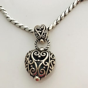 May include: A silver-toned necklace featuring a heart-shaped pendant with intricate scrollwork and cut-out details. The pendant hangs from a twisted silver-toned chain by a matching decorative bail, showcasing a polished metallic finish.