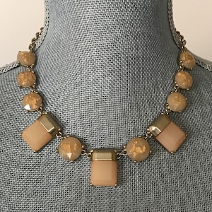 May include: A white ceramic mug with a black handle and the text "But First, Coffee" in a bold, black font. The mug is set against a blurred background, suggesting a cozy setting.