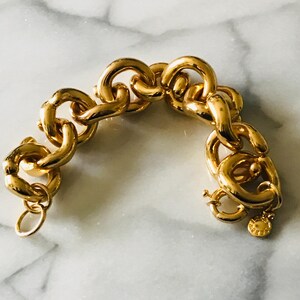 May include: A gold-toned chain bracelet with large, rounded links. The bracelet has a lobster clasp closure and a small charm. The jewelry is displayed on a marble surface. The bracelet is approximately 7 inches in length.