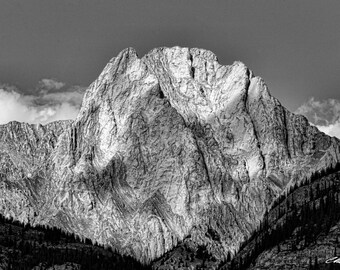 May include: A black and white photograph of a large, rocky mountain peak with a cloudy sky in the background.