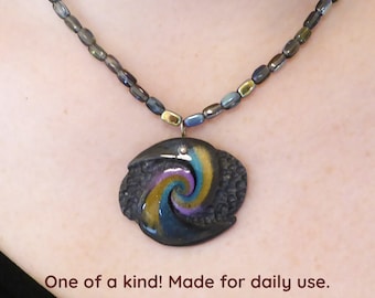 Carved gray polymer clay with a swirl of gold and other metallic colors. Dom of resin. Silver colored clasp and chain. Free form necklace.