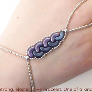 以下が含まれることがあります： 紫と青のビーズのデザインが施されたシルバーチェーンブレスレット。ブレスレットは伸縮性があり、指にループがあります。