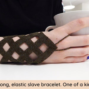 May include: A brown beaded slave bracelet with a geometric design. The bracelet is elastic and has a long chain that extends from the wrist to the fingers.