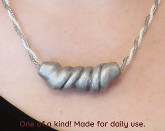 A twisted 3D tube of silver colored polymer clay. Chain with gray and white seed beads. Nickel free silver colored clasp & chain. Free form