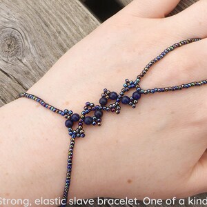 May include: A dark blue elastic slave bracelet with a beaded design. The bracelet is made with small, iridescent beads and features a delicate, intricate pattern.