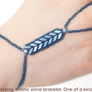 以下が含まれることがあります： 青いビーズと銀色のビーズでできた、伸縮性のあるスレーブブレスレット。ブレスレットは、ユニークな織り模様が施されています。