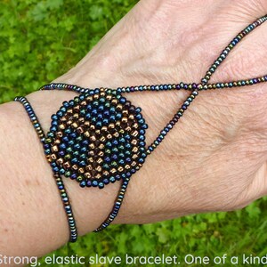 May include: A dark blue and bronze beaded bracelet with an elastic band. The bracelet has a large circular design in the center.