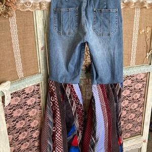 Pode incluir: Jeans de sino azul de ganga com uma cintura vermelha "Tommy Jeans". A parte inferior das cal&ccedil;as &eacute; feita de um mosaico de gravatas coloridas.