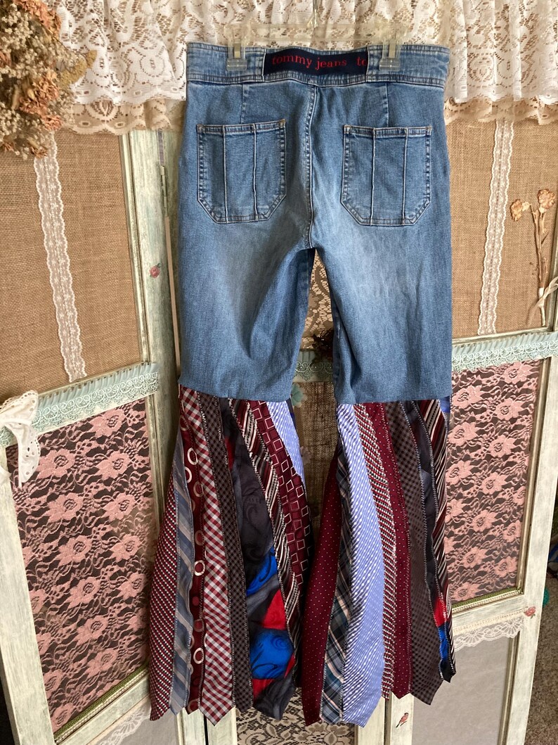 Pode incluir: Jeans de sino azul de ganga com uma cintura vermelha "Tommy Jeans". A parte inferior das cal&ccedil;as &eacute; feita de um mosaico de gravatas coloridas.