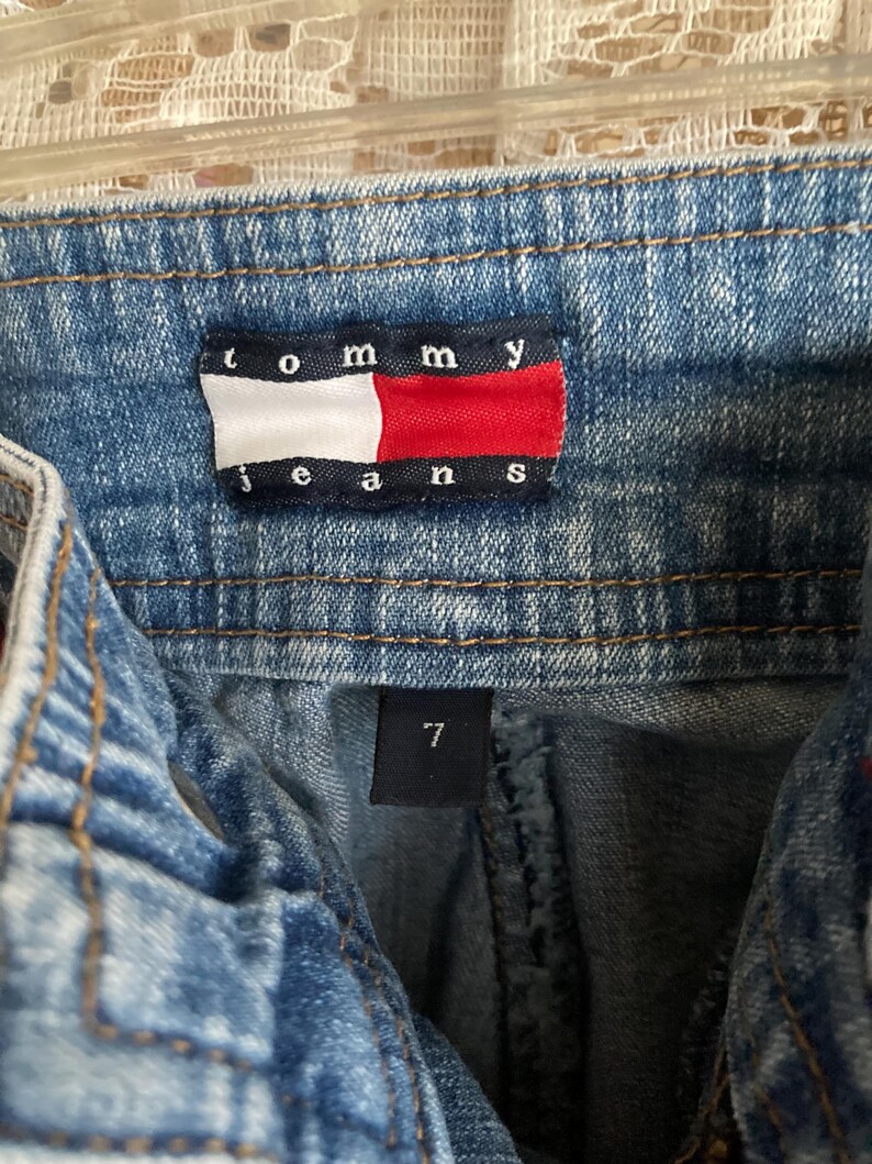 Pode incluir: Um par de cal&ccedil;as de ganga azuis com uma etiqueta Tommy Jeans e uma etiqueta de tamanho 7.