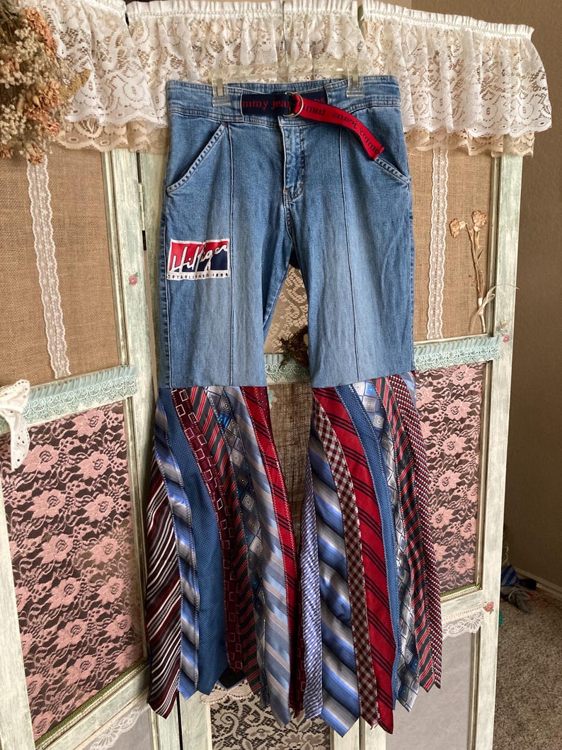 Pode incluir: Jeans azul denim com um cinto vermelho e azul e um padr&atilde;o tie-dye feito de gravatas. O jeans tem um patch com o logotipo da Tommy Jeans na perna esquerda.